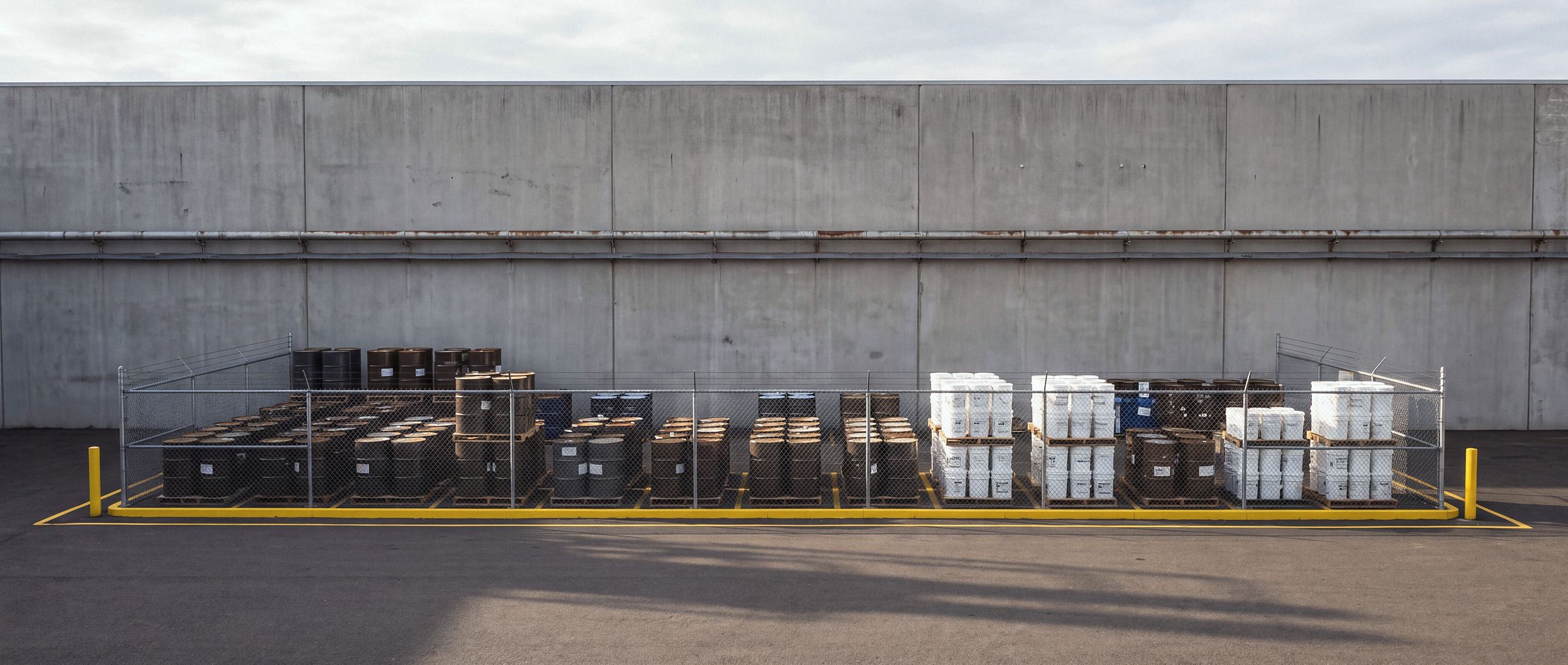 Pátio industrial com tambores e baldes organizados em paletes para coleta e retorno.