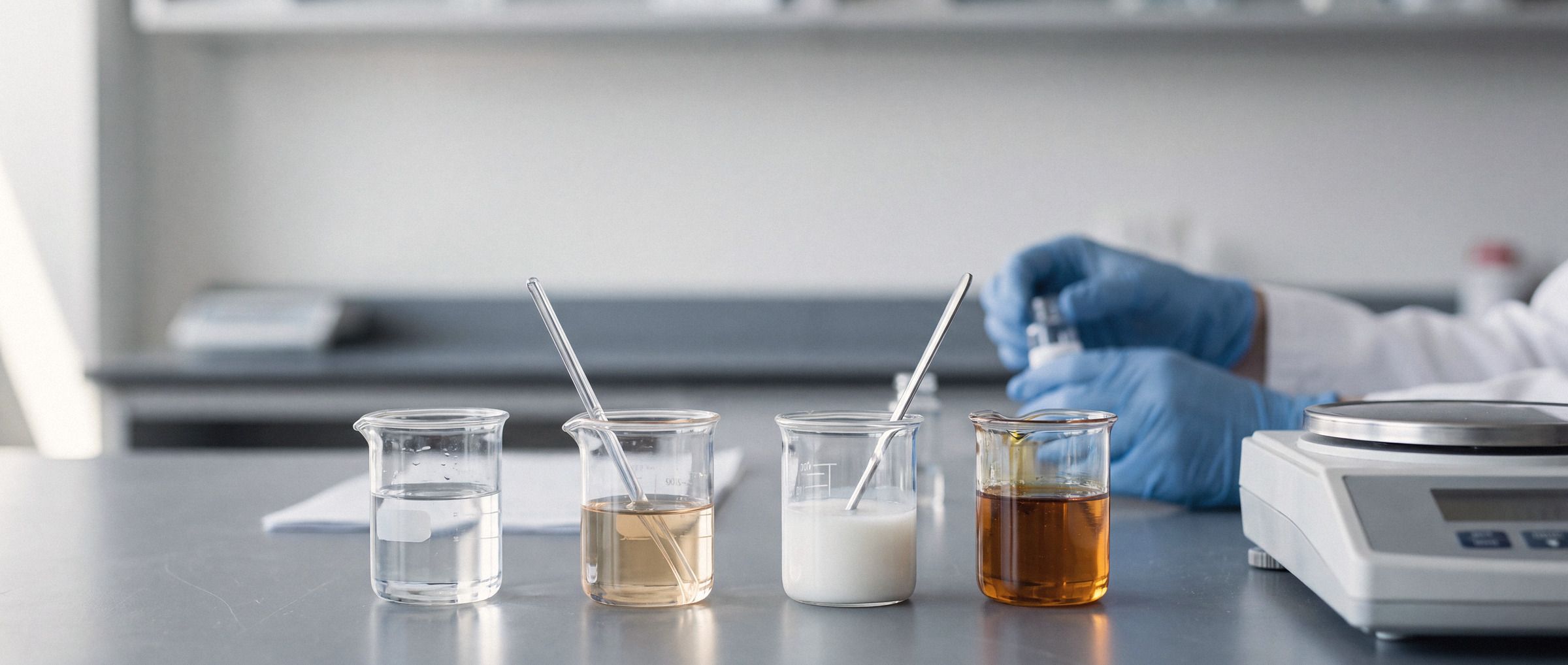 Bancada de laboratório com amostras de fluidos de diferentes cores e viscosidades em béqueres.